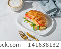 A golden croissant sandwich with ham, cheese, tomato, and arugula on a marble background 141638132