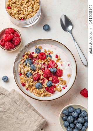 Natural greek yogurt with granola, blueberry and raspberry in a bowl on a light textured background Natural greek yogurt with granola, blueberry and raspberry in a bowl on a light textured background 141638143