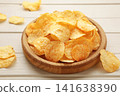 Potato chips on wooden plate on white wooden background 141638390