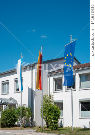Bavarian, German and European Union flags on flagpoles in front of office building on sunny day in Germany Bavarian, German and European Union flags on flagpoles in front of office building on sunny day in Germany 141638436