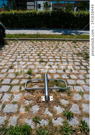 Folded down parking barrier on paved parking lot with dry grass and weeds in summer, broken metal post on ground in Germany Folded down parking barrier on paved parking lot with dry grass and weeds in summer, broken metal post on ground in Germany 141638444