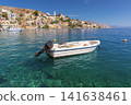 Small Motor Boat Anchored off Symi Harbor with Waterfront Town in Greece 141638461