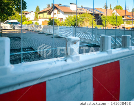 Construction site barrier with red and white warning stripes in residential street in Germany, safety fence in front of new building area on sunny day Construction site barrier with red and white warning stripes in residential street in Germany, safety fence in front of new building area on sunny day 141638498