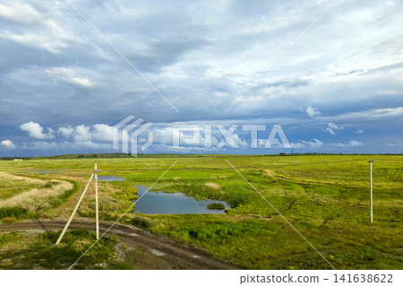 View from train window passing vast green fields with puddle and dirt road - rural Ukrainian landscape View from train window passing vast green fields with puddle and dirt road - rural Ukrainian landscape 141638622