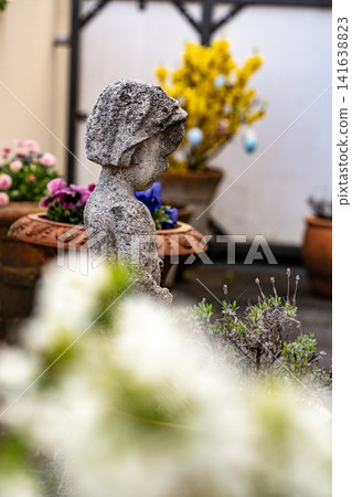 Stone Garden Statue Surrounded By Spring Flowers: Cozy Patio With Chrysanthemum And Geranium Plants Stone Garden Statue Surrounded By Spring Flowers: Cozy Patio With Chrysanthemum And Geranium Plants 141638823
