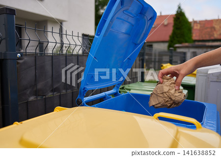 Woman placing paper packaging into blue recycling bin outside home Woman placing paper packaging into blue recycling bin outside home 141638852