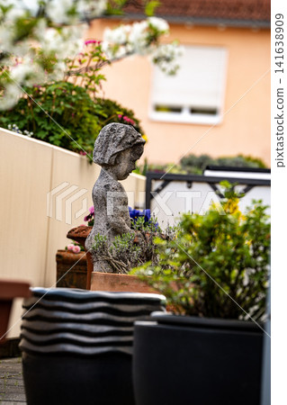 Stone Garden Statue Surrounded By Spring Flowers: Cozy Patio With Chrysanthemum And Geranium Plants Stone Garden Statue Surrounded By Spring Flowers: Cozy Patio With Chrysanthemum And Geranium Plants 141638909