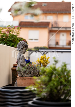 Stone Garden Statue Surrounded By Spring Flowers: Cozy Patio With Chrysanthemum And Geranium Plants Stone Garden Statue Surrounded By Spring Flowers: Cozy Patio With Chrysanthemum And Geranium Plants 141638944