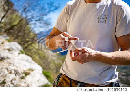Male Climber Taping Fingers Before Route: Close Up Of Hands Preparing For Outdoor Rock Climbing Male Climber Taping Fingers Before Route: Close Up Of Hands Preparing For Outdoor Rock Climbing 141639110