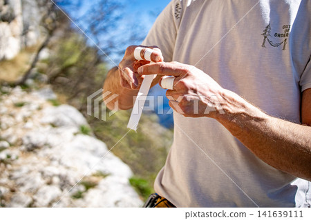 Male Climber Taping Fingers Before Route: Close Up Of Hands Preparing For Outdoor Rock Climbing Male Climber Taping Fingers Before Route: Close Up Of Hands Preparing For Outdoor Rock Climbing 141639111