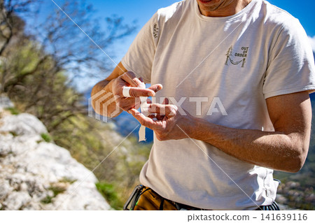 Male Climber Taping Fingers Before Route: Close Up Of Hands Preparing For Outdoor Rock Climbing Male Climber Taping Fingers Before Route: Close Up Of Hands Preparing For Outdoor Rock Climbing 141639116