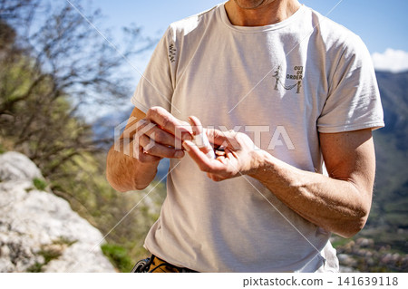Male Climber Taping Fingers Before Route: Close Up Of Hands Preparing For Outdoor Rock Climbing Male Climber Taping Fingers Before Route: Close Up Of Hands Preparing For Outdoor Rock Climbing 141639118