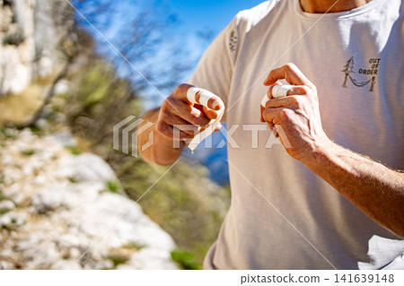 Male Climber Taping Fingers Before Route: Close Up Of Hands Preparing For Outdoor Rock Climbing 141639148