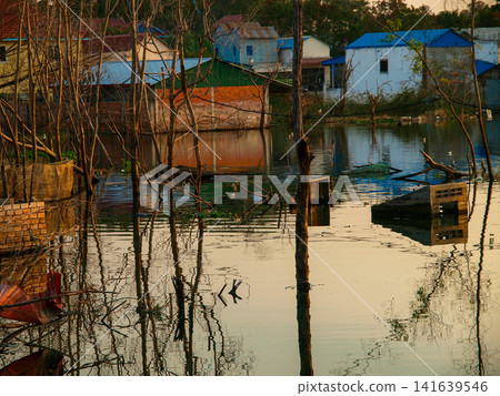 Traditional stilt houses and structures reflected in calm water during golden hour in a rural village near Phnom Penh, Cambodia Traditional stilt houses and structures reflected in calm water during golden hour in a rural village near Phnom Penh, Cambodia 141639546