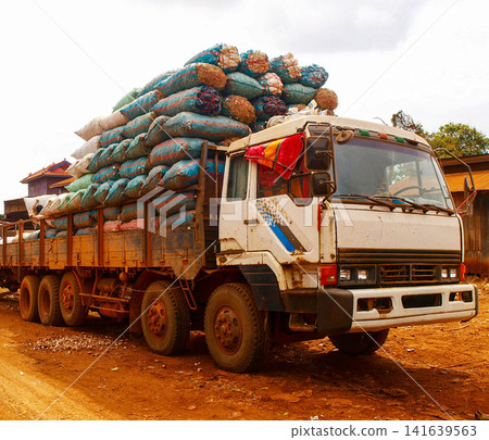 Heavy Cargo Truck Loaded With Stacked Sacks: Rural Freight Transportation On Dirt Road In Cambodia Southeast Asia Heavy Cargo Truck Loaded With Stacked Sacks: Rural Freight Transportation On Dirt Road In Cambodia Southeast Asia 141639563