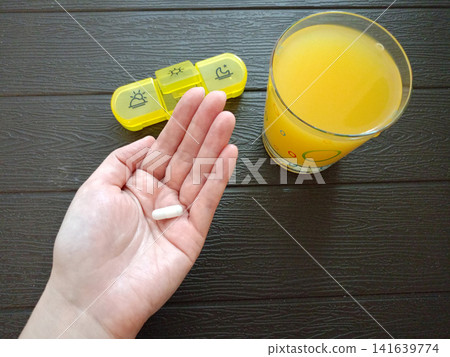A woman's hand holding an iron capsule and a glass of orange juice A woman's hand holding an iron capsule and a glass of orange juice 141639774