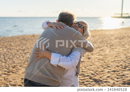 Senior mature couple hugging enjoying outdoor recreation walking on beach. Old husband wife embracing with tenderness love enjoying sweet bonding. Grandmother grandfather together. Family moment love Senior mature couple hugging enjoying outdoor recreation walking on beach. Old husband wife embracing with tenderness love enjoying sweet bonding. Grandmother grandfather together. Family moment love 141640528