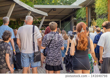 Crowd of visitors stands outside venue, public event, view from behind. People gathers near entrance, attendees watch activity, record video, wait together Crowd of visitors stands outside venue, public event, view from behind. People gathers near entrance, attendees watch activity, record video, wait together 141640798