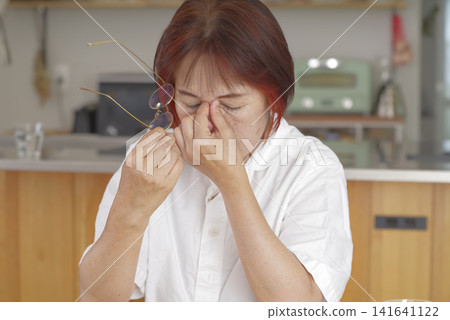 A senior woman takes off her reading glasses to rest her eyes. A senior woman takes off her reading glasses to rest her eyes. 141641122