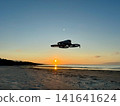 Silhouette of Flying Drone Over Beach at Sunset by the Sea 141641624