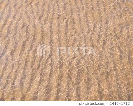 Crystal clear shallow ocean water flowing over golden ribbed sand, creating a serene, meditative ripple pattern. A calm nature scene, no people, capturing the peaceful essence of a summer beach. Crystal clear shallow ocean water flowing over golden ribbed sand, creating a serene, meditative ripple pattern. A calm nature scene, no people, capturing the peaceful essence of a summer beach. 141641712
