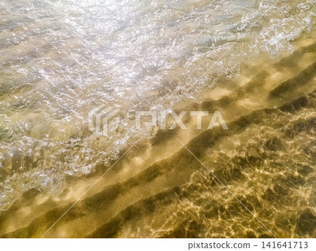 A sparkling crystalclear ocean wave gently rolls onto a sandy beach, evoking peace and summer relaxation. No people. A bright, sunlit coastal scene perfect for nature, travel, or serene concepts. A sparkling crystalclear ocean wave gently rolls onto a sandy beach, evoking peace and summer relaxation. No people. A bright, sunlit coastal scene perfect for nature, travel, or serene concepts. 141641713