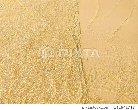 Clear tropical water gently washes over golden sand in this serene beach scene, featuring no people. The tranquil ripple effect evokes feelings of summer relaxation, peace, and coastal beauty. Clear tropical water gently washes over golden sand in this serene beach scene, featuring no people. The tranquil ripple effect evokes feelings of summer relaxation, peace, and coastal beauty. 141641718