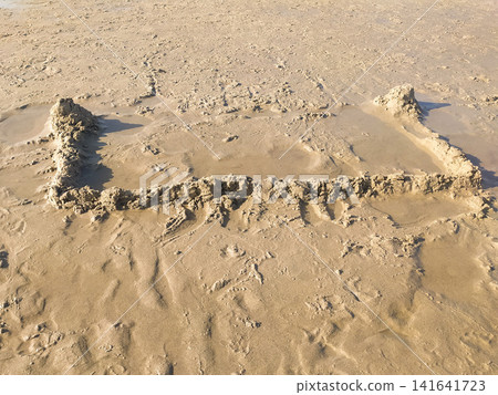 A simple sand castle foundation sits on a quiet beach, no people present. This peaceful scene evokes childhood nostalgia, innocence, and summer memories. Perfect for travel or lifestyle concepts. 141641723