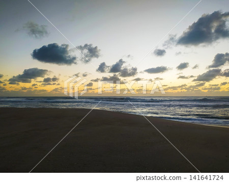 Captivating sunrise over a tranquil beach with rolling ocean waves and dramatic clouds. This serene coastal landscape is perfect for travel, wellness, and environmental themes. Purely stunning. 141641724