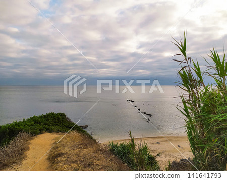 A serene, tranquil coastal view overlooking a peaceful sandy beach and calm ocean at twilight. Nobody present, this scenic landscape captures the quiet solitude and natural beauty of the shore. A serene, tranquil coastal view overlooking a peaceful sandy beach and calm ocean at twilight. Nobody present, this scenic landscape captures the quiet solitude and natural beauty of the shore. 141641793