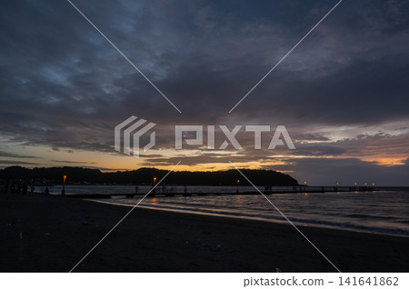The lights of the pier and the lingering glow of the sunset are reflected on the twilight sea (by the sea). The lights of the pier and the lingering glow of the sunset are reflected on the twilight sea (by the sea). 141641862