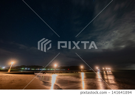 A starry night sky and the streetlights of the pier glinting on the beach. 141641894