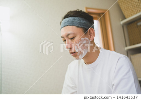 一名四十多歲的男子在浴室裡低著頭,用泡沫洗臉。 一名四十多歲的男子在浴室裡低著頭,用泡沫洗臉。 141643537