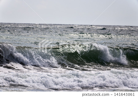 Waves crashing against the shore, sending up white spray. 141643861