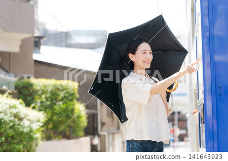 在炎熱的夏天，一位女士在自動販賣機購買飲料。 141643923