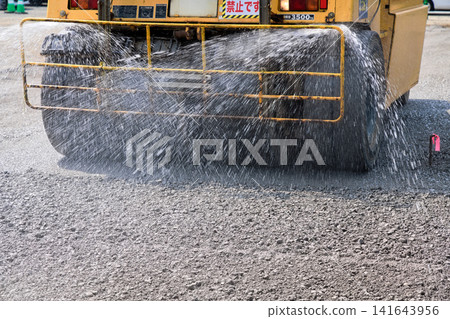 停車場施工:使用壓路機進行地面壓實作業,同時進行灑水作業。 停車場施工:使用壓路機進行地面壓實作業,同時進行灑水作業。 141643956