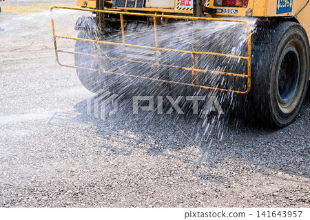 停車場施工:使用壓路機進行地面壓實作業,同時進行灑水作業。 停車場施工:使用壓路機進行地面壓實作業,同時進行灑水作業。 141643957