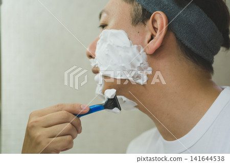 Close-up of a 40-year-old man applying shaving foam and shaving his neck and chin with a razor. Close-up of a 40-year-old man applying shaving foam and shaving his neck and chin with a razor. 141644538