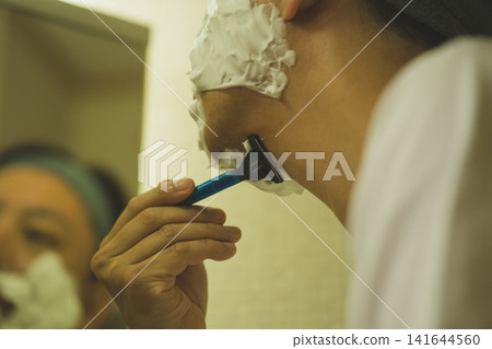 A man in his 40s shaves against the grain under his chin with a razor in the bathroom. (From behind) A man in his 40s shaves against the grain under his chin with a razor in the bathroom. (From behind) 141644560