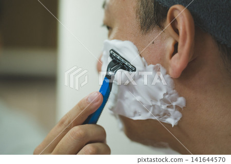 Close-up of a 40-year-old man shaving his cheeks and sideburns with a razor. Close-up of a 40-year-old man shaving his cheeks and sideburns with a razor. 141644570