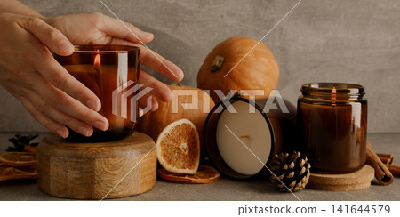 Candles on wooden stands, pumpkins and female hands on gray back Candles on wooden stands, pumpkins and female hands on gray back 141644579