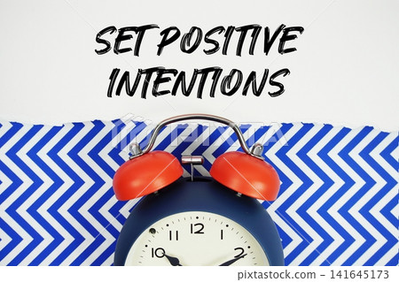 Set Positive Intentions text written on paper with alarm clock on blue chevron background Set Positive Intentions text written on paper with alarm clock on blue chevron background 141645173