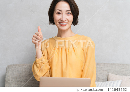 Woman sitting on the sofa and using a laptop Lifestyle image Woman sitting on the sofa and using a laptop Lifestyle image 141645362