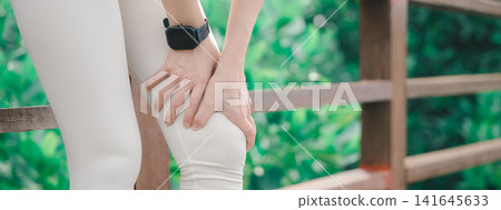 Female runner experiencing sudden knee, injury, pain during outdoor workout, athletic woman clutching sore joint while standing on wooden bridge in park with lush green background Female runner experiencing sudden knee, injury, pain during outdoor workout, athletic woman clutching sore joint while standing on wooden bridge in park with lush green background 141645633