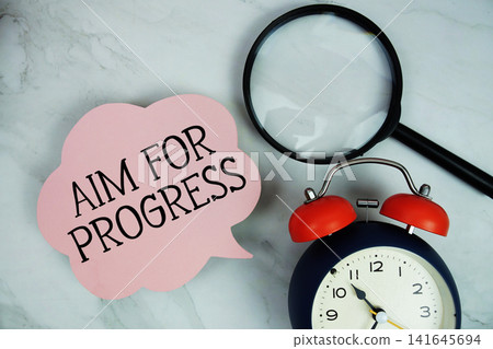 Aim For Progress text with magnifying glass and alarm clock on marble background Aim For Progress text with magnifying glass and alarm clock on marble background 141645694