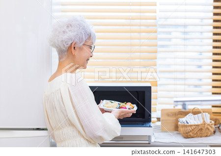 用餐:老年婦女在家中加熱她們自備的午餐。 用餐:老年婦女在家中加熱她們自備的午餐。 141647303