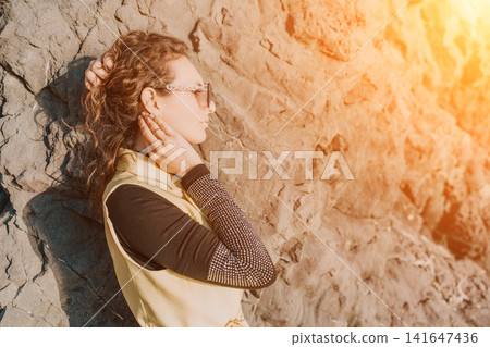 Woman profile rock portrait of traveler wearing sunglasses leaning against textured stone wall during sunset 141647436