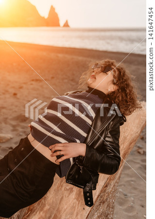 Woman Sunset Beach young woman relaxing on a driftwood log at the shore during sunset enjoying a serene mood Woman Sunset Beach young woman relaxing on a driftwood log at the shore during sunset enjoying a serene mood 141647454