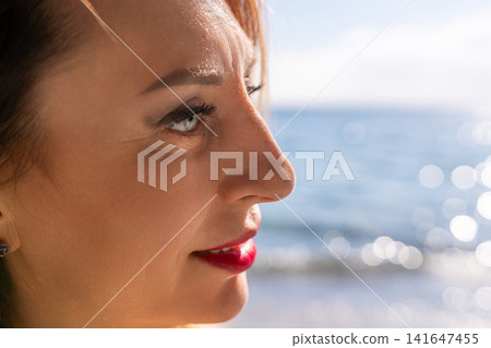 Woman beach profile side view of a beautiful middle aged woman looking at the sparkling blue ocean with copy space Woman beach profile side view of a beautiful middle aged woman looking at the sparkling blue ocean with copy space 141647455