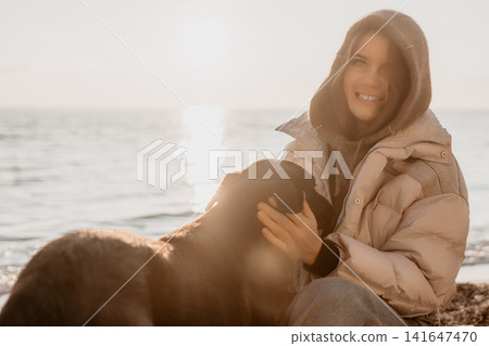 Woman, dog, beach smiling woman petting dark dog on the seashore during golden hour sunset Woman, dog, beach smiling woman petting dark dog on the seashore during golden hour sunset 141647470